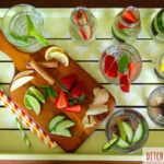 A serving tray showing flavoured water ideas with strawberries cucumber ginger and limes