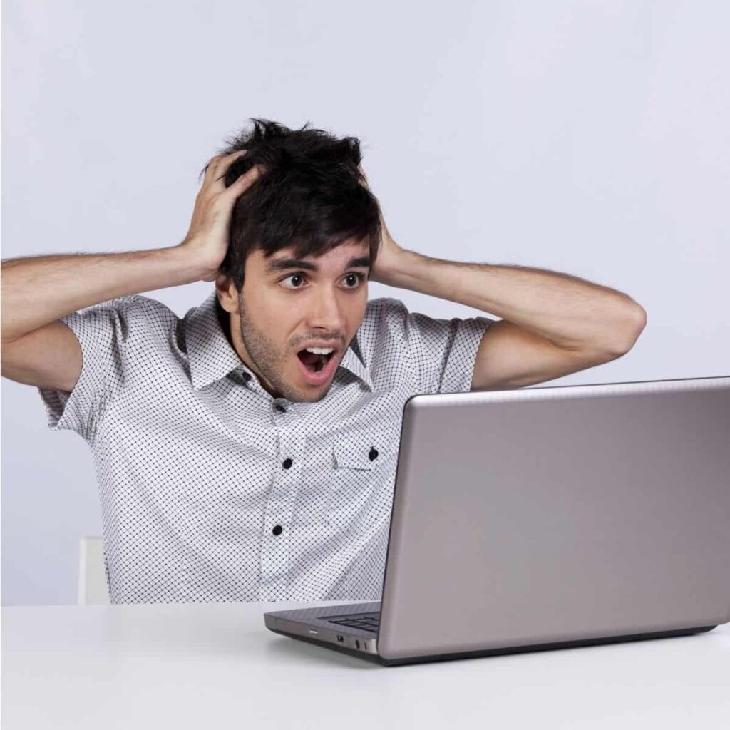 A person holding his head in his hands in front of a laptop