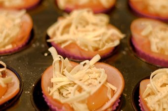 Ham and egg cups sitting in a muffin tray covered with shredded cheese