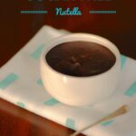 A white dish with sugar free nutella on a blue cloth and dark wooden table
