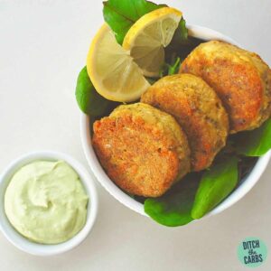 salmon patties with lime avocado dressing served in a white bowl with baby spinach