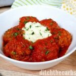 Instant pot meatballs served in a white bowl with cream cheese and garnished with herbs