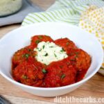 And white bowl of self saucing instant pot meatballs garnished with sour cream and herbs