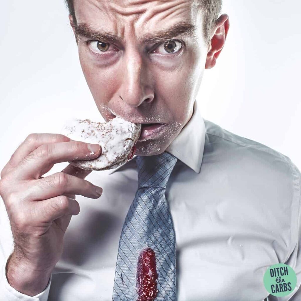 A man eating a doughnut with jam dripping down his tie