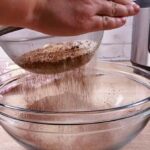 Hands sifting low carb flour and cocoa powder into a glass bowl