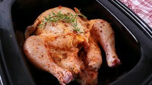 Whole chicken seasoned with herbs and sitting in the slow cooker
