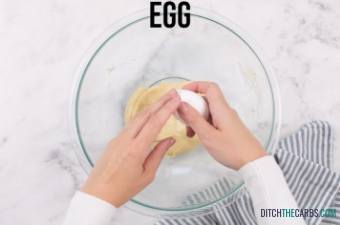 Hands placing a cracked egg into a mixing bowl