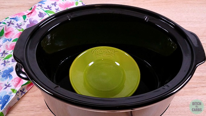 Slow cooker with a green dish inside to raise the cheesecake tin when cooking