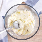 Ricotta cheese and parmesan cheese mixed together in a clear glass bowl.