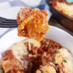 A bite of low-carb skillet lasagna being lifted from a white bowl full of lasagna.