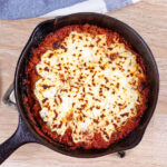 Low-carb skillet lasagna has been cooked in the skillet and is cooking on the counter. The top of the lasagna has been browned.