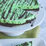 No-Bake Sugar-Free Mint Cheesecake drizzled with chocolate sliced and served on a white cake stand