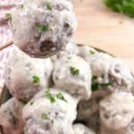 Creamy goat cheese keto meatballs in a bowl. One meatball is being lifted by a toothpick.