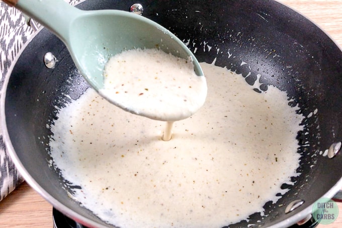 Creamy goat cheese sauce being mixed in a pan. The spoon is lifted to show the thick sauce pour off a light green spoon.