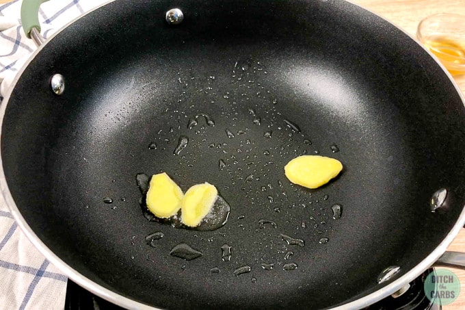 Sautéing 3 slices of ginger in hot oil using a black skilet.