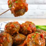 Spicy garlic keto meatballs in a bowl. One meatball is being lifted by a toothpick.