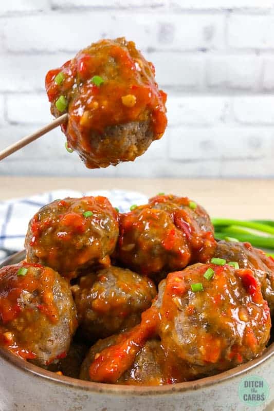 Spicy garlic keto meatballs in a bowl. One meatball is being lifted by a toothpick.