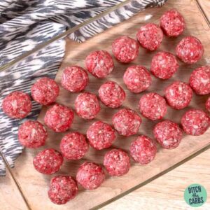 Keto meatballs shaped into balls and arranged in a clear glass baking pan.