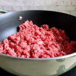 Uncooked ground beef in a green skillet being browned for keto Taco Bell meat.
