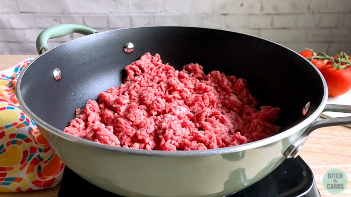 Uncooked ground beef in a green skillet being browned for keto Taco Bell meat.