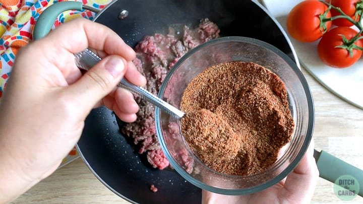 Scooping taco seasoning over ground beef for keto Taco Bell.