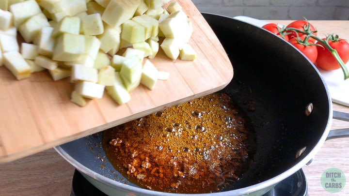 Pouring peeled and cubed eggplant into a skillet with grease from the taco meat still in the pan.