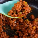 Scooping low-carb Sloppy Joes meat out of a skillet with a light blue spoon.