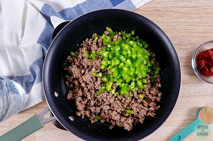 Browned ground beef and chopped green bell pepper in a skillet.