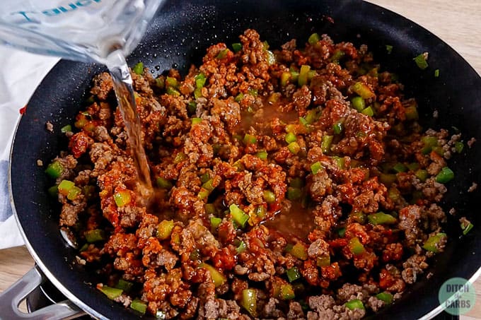 Pouring water into low-carb Sloppy Joe meat in a skillet to make the meat saucy.
