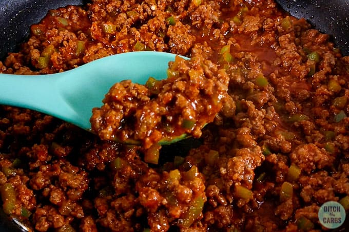 Low-carb Sloppy Joe meat in a skillet being scooped with a light blue spoon.