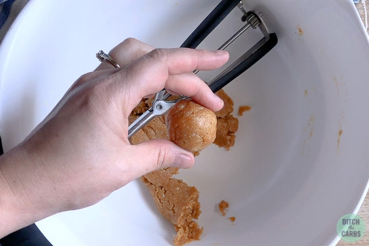 Hands rolling a ball of peanut butter cookie dough