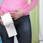 woman in blue jeans with tummy cramp and toilet paper