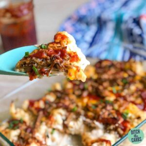 A close up of keto pulled pork mac and cheese being served from a glass serving dish