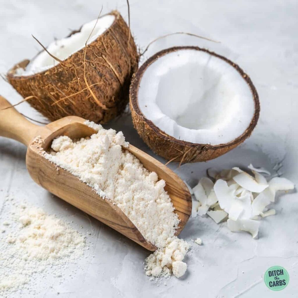 coconut flour in wooden scooper near open coconut and shredded coconut
