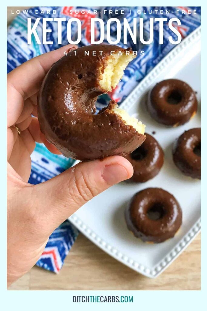A hand is lifting a almond flour keto donut with a bite taken out up