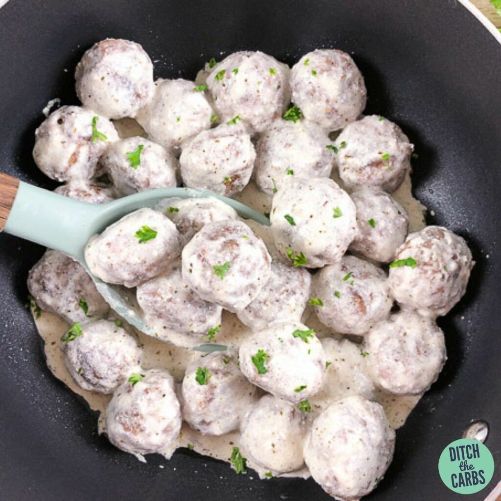 Keto goat cheese meatballs in a skillet with a spoon lifting a serving of meatballs.