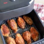 Chicken wings tossed in dry rub seasoning arranged in the basket of the air fryer ready to be cooked.