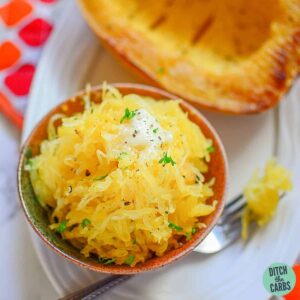 Spaghetti squash being lifted from the serving bowl with a fork