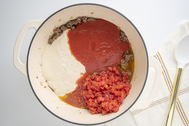 Adding alfredo sauce, tomatoes, and tomato sauce to the meat mixture. 