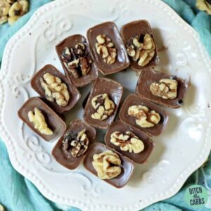 A pile of chocolate fat bombs sitting on a white plate and decorated with walnuts