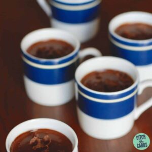 Small sugar-free mocha cups on a wooden table decorated with shaved pieces of chocolate