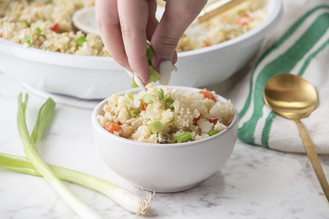 Sprinkling green onions on top of a bowl of cauliflower fried rice 