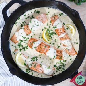 Keto salmon recipe in a creamy butter garlic sauce. Topped with parsley and fresh lemon slices.