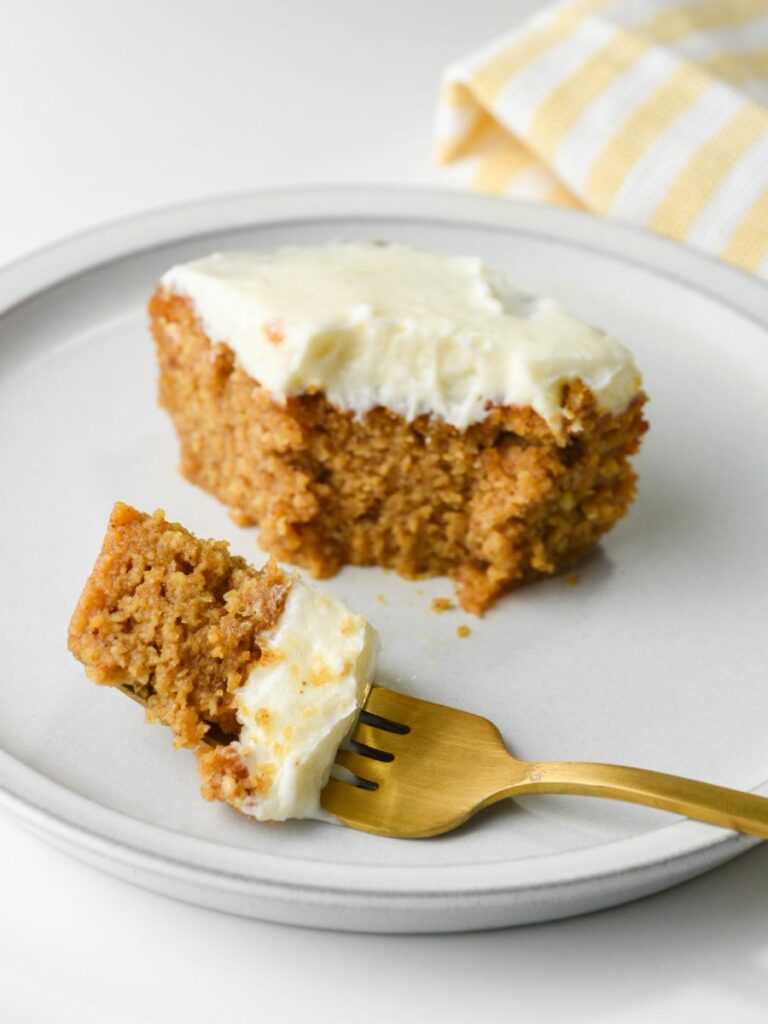 A slice of pumpkin bars with cream cheese frosting on a small white plate - a small bite is on a fork