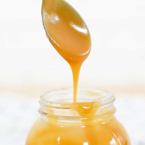 A spoon drizzling a spoonful of sugar-free keto caramel sauce into the jar of caramel.