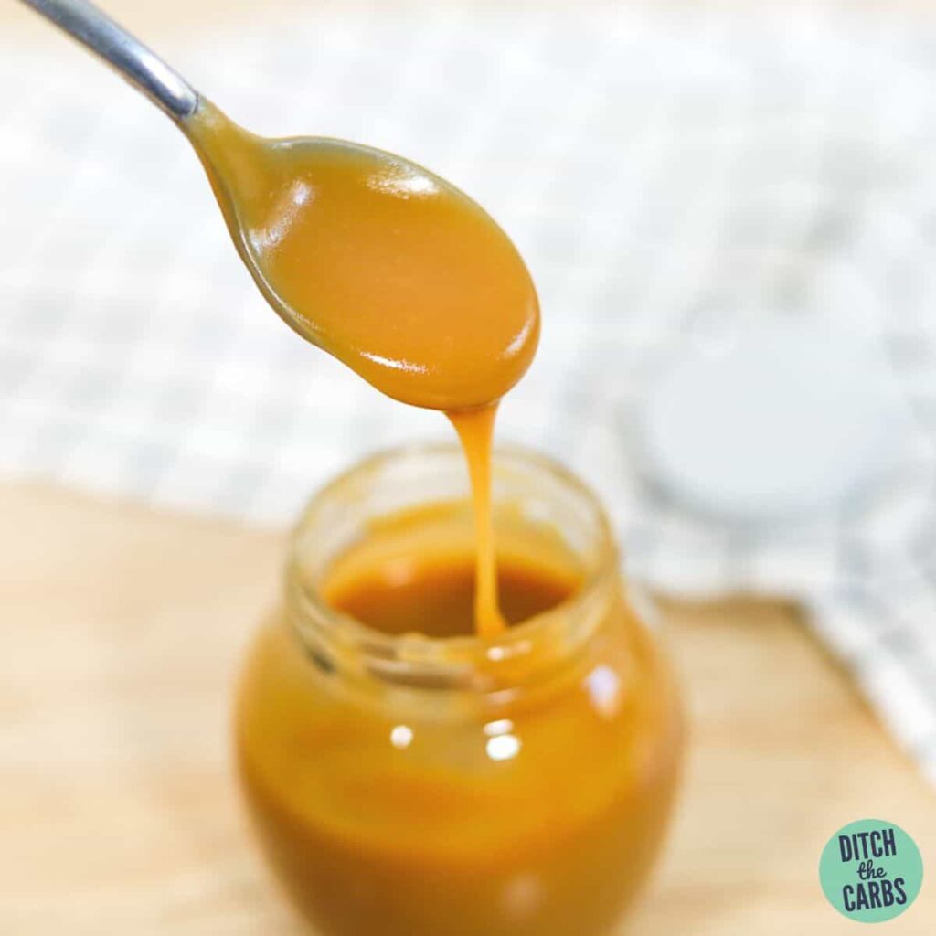 A spoon drizzling a spoonful of sugar-free keto caramel sauce into the jar of caramel.