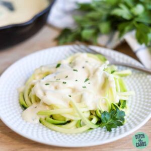 Zucchini noodles on a plate covered with keto alfredo sauce.