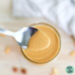 A spoon lifting a spoonful of keto peanut butter from a jar.