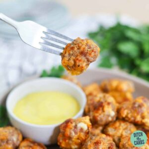 A fork dipping a keto sausage ball in mustard.