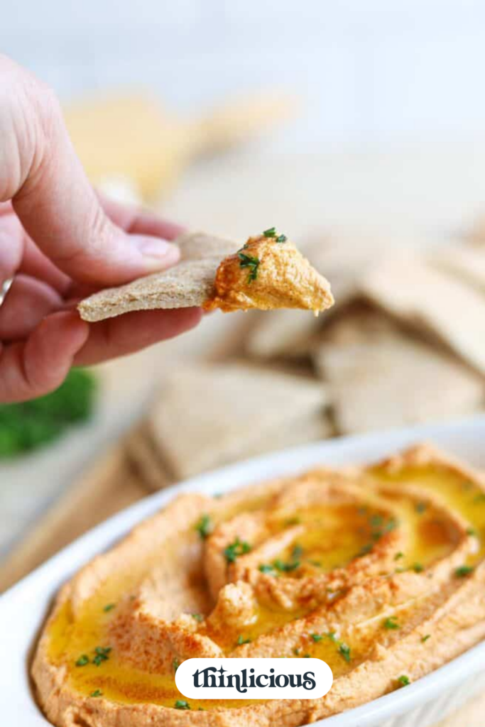 A hand lifting a piece of low-carb pita bread that was just dipped into low-carb hummus.